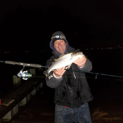 Nick Honachefsky holding a fishing rod and a striped bass at night