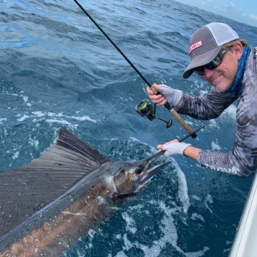 A man leaning over a boat holding a fishing rod and the bill of a sailfish