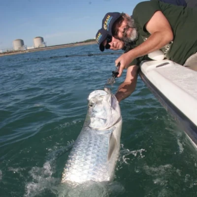 A man leaning over a boat holding a tarpon fish
