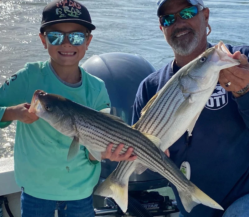 A kid and a guy both holding striped bass