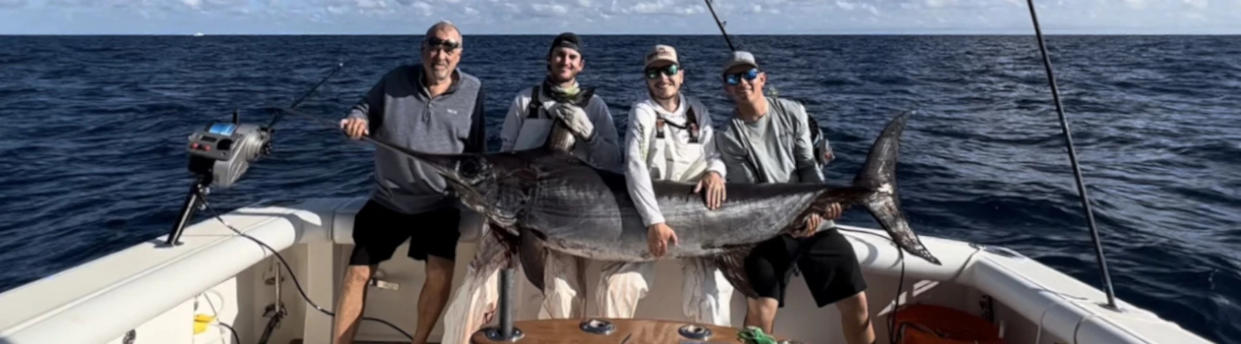 four anglers on a boat holding a swordfish